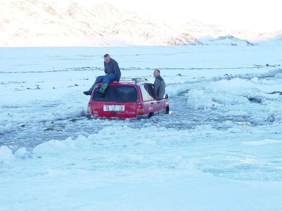 Red Jeep Grand Cherokee stuck in icy water, two men on and in the vehicle