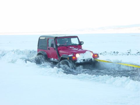 2001 Jeep Wrangler - A red Jeep Wrangler is stuck in deep snow and water, with a yellow strap attached to the front.