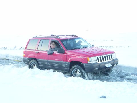 2001 Jeep Wrangler - Red Jeep Grand Cherokee struggles through deep snow and ice, with water spraying from its tires.