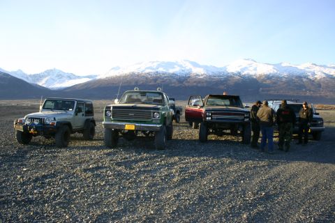 2003 Jeep TJ - A silver Jeep TJ is parked on a gravel lot with other vehicles, facing snow-covered mountains.