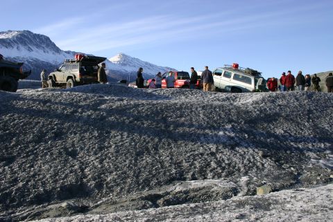 2003 Jeep TJ - A group of people and several off-road vehicles are gathered on a rocky, icy terrain with snow-covered mountains under a clear blue sky.