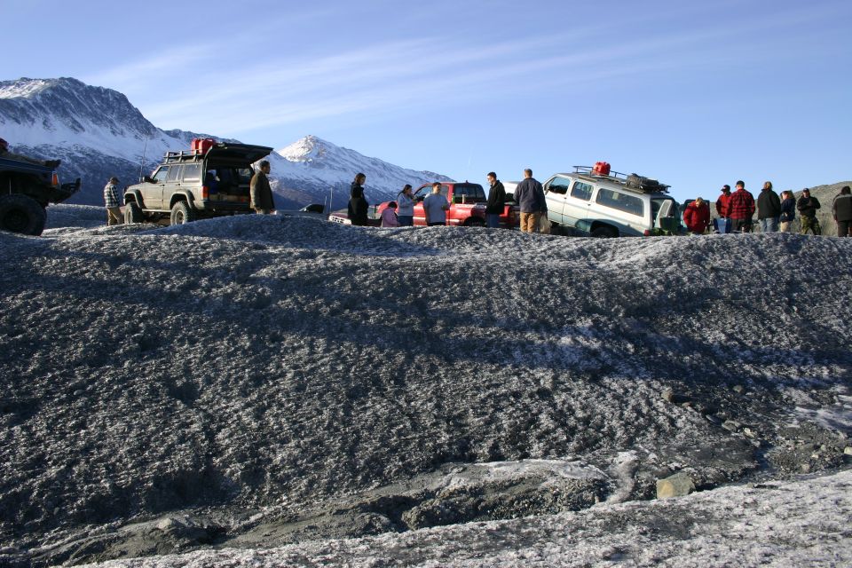 2003 Jeep TJ and other off-road vehicles on a rocky, icy surface with people gathered around, snow-capped mountains in the distance