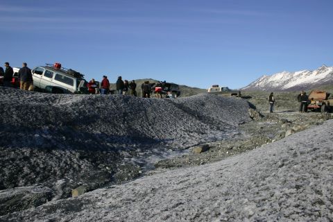 2003 Jeep TJ - Several off-road vehicles are parked on a glacier, with a group of people gathered around them under a clear blue sky.