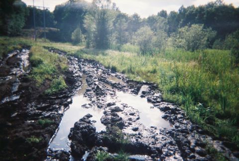 2000 Chevrolet Tahoe - Muddy track with puddles and grass on the sides, trees in the background. Supermotors.net logo in corner.