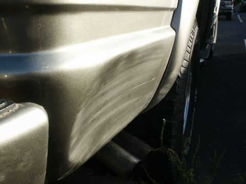 2000 Chevrolet Tahoe - The rear of a vehicle shows scuff marks and dual exhaust pipes, with another vehicle in the distance.