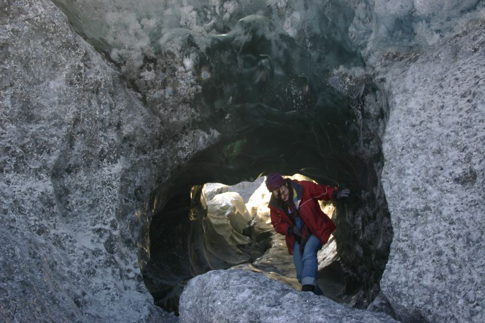 Person in red jacket and blue jeans stands in an ice cave entrance
