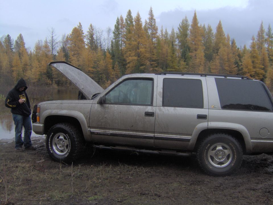 2000 Chevrolet Tahoe parked on muddy ground with hood open, person in hoodie standing beside it