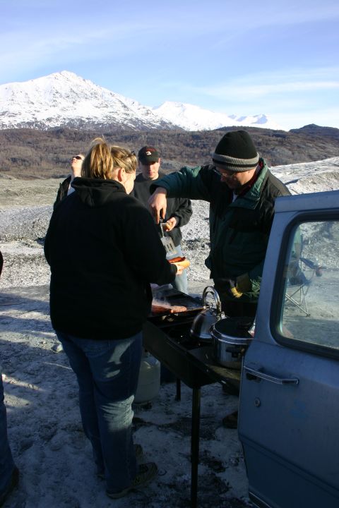 2003 Jeep TJ - People gather around a grill in a snowy landscape with mountains visible under a clear blue sky.
