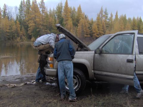 2000 Chevrolet Tahoe - Two people inspect the engine of a muddy 2000 Chevrolet Tahoe near a body of water.