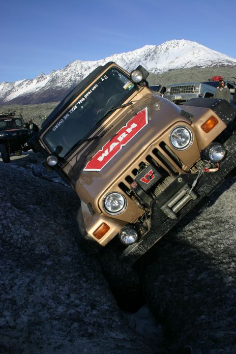 2003 Jeep TJ - A gold 2003 Jeep TJ with a WARN winch navigates challenging terrain near snow-capped mountains.