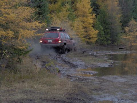 2000 Chevrolet Tahoe - Red Jeep Grand Cherokee navigates a muddy trail during autumn.