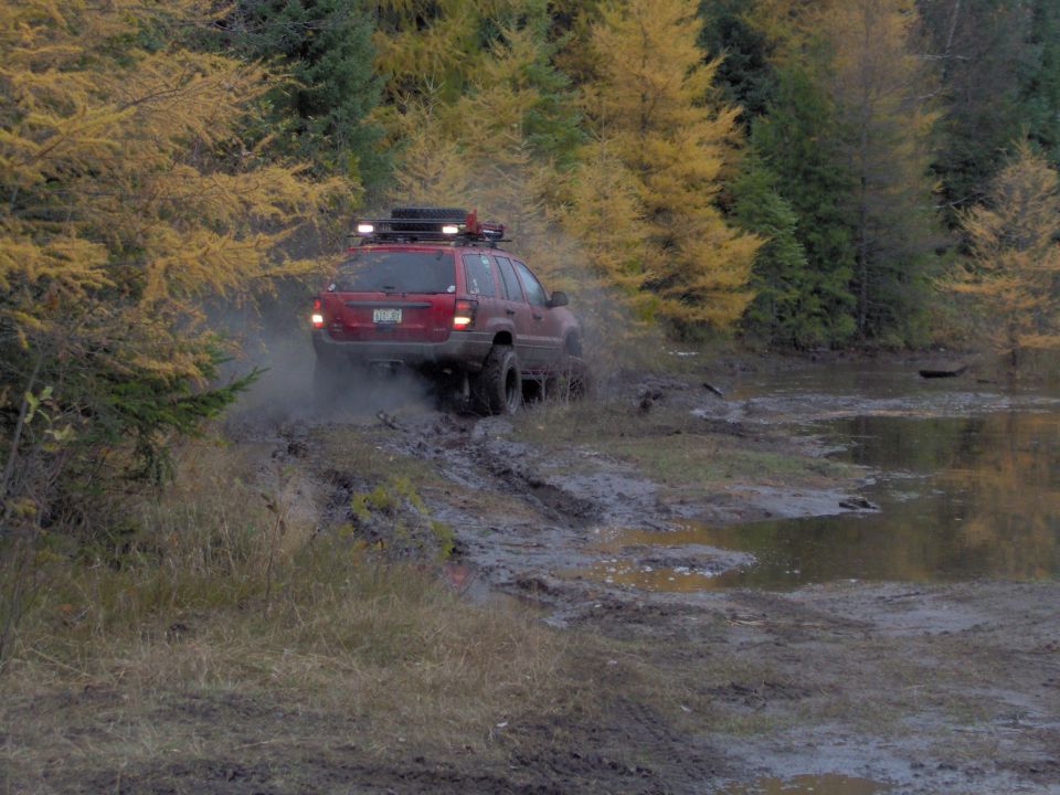 Red Jeep Grand Cherokee driving through mud with roof rack