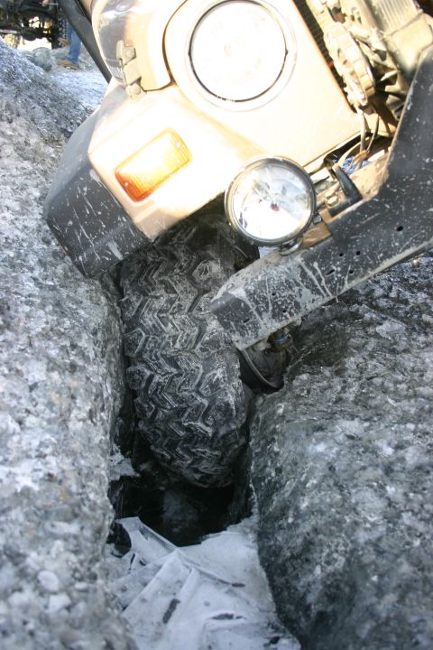 2003 Jeep TJ - A Jeep Wrangler's front tire is wedged in a deep, icy crevice on a rocky terrain.