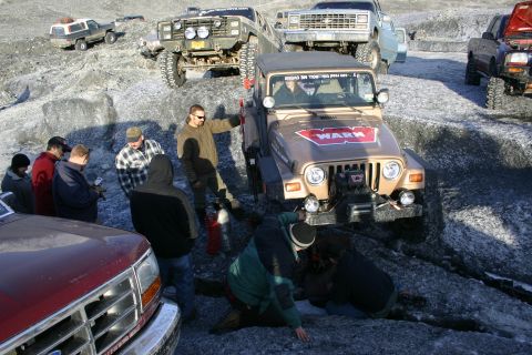 2003 Jeep TJ - Multiple off-road vehicles gathered on a rocky, icy surface, with people interacting around a tan Jeep Wrangler.