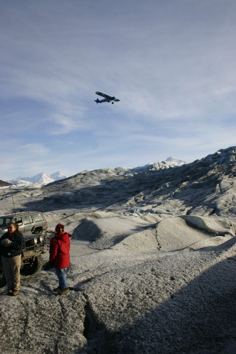 2003 Jeep TJ - Two people stand next to a Jeep Wrangler on a glacier, with a small airplane flying in the sky above the icy terrain.