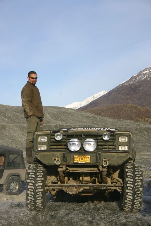 2003 Jeep TJ - A man poses on a heavily modified off-road truck in a rocky, mountainous terrain under a clear sky.