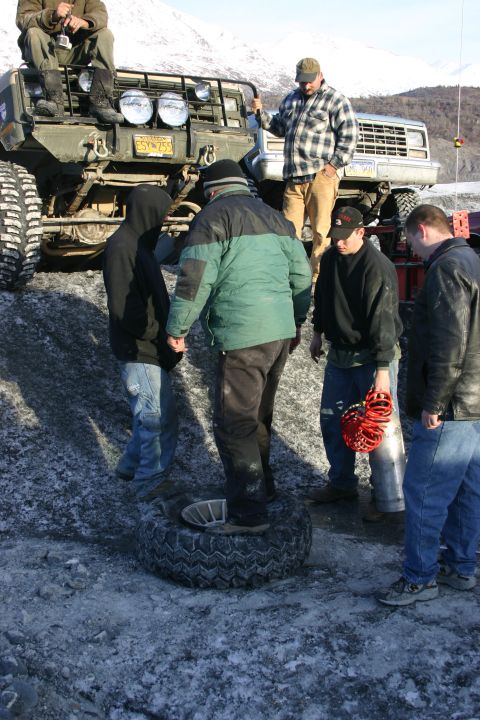 2003 Jeep TJ - A group of people are gathered around a spare tire in front of a green Jeep Wrangler, possibly preparing for off-road conditions.