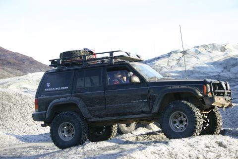 2003 Jeep TJ - A black Jeep Cherokee XJ navigates a snowy, icy terrain with a glacier in the background.