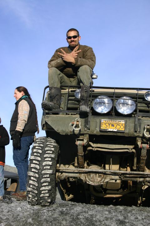 2003 Jeep TJ - Man sits on the hood of a military truck with an Alaska license plate.