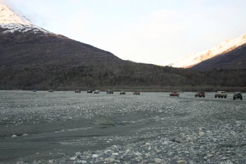 2003 Jeep TJ - A convoy of 2003 Jeep TJs navigates a wide, rocky riverbed beneath imposing, snow-dusted mountains.