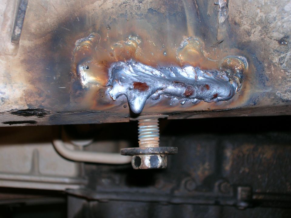 close-up of a rough weld on a vehicle frame with a bolt and washer below it