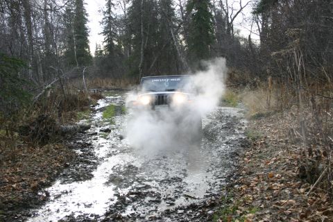 2003 Jeep TJ - Jeep TJ navigates a muddy, wooded path, kicking up steam.