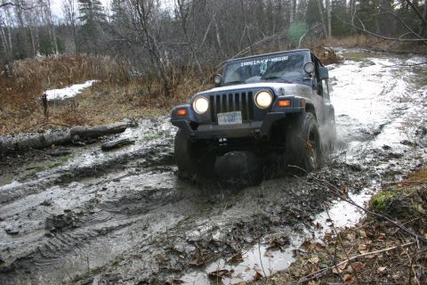 2003 Jeep TJ - A Jeep Wrangler TJ navigates a muddy trail in a wooded area.