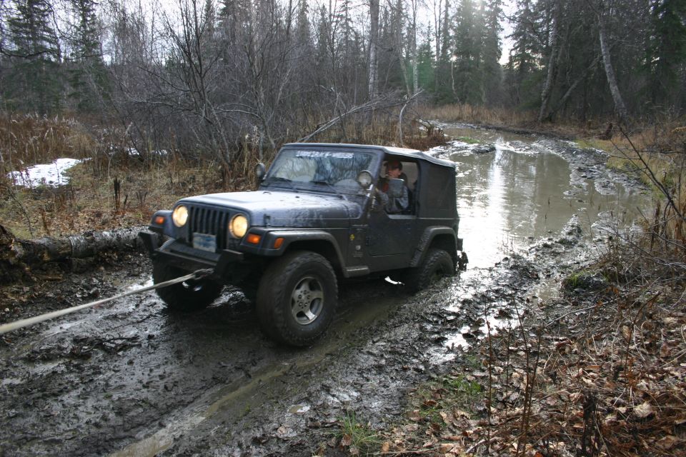 Dark blue 2003 Jeep TJ stuck in a muddy trail, being pulled by a rope
