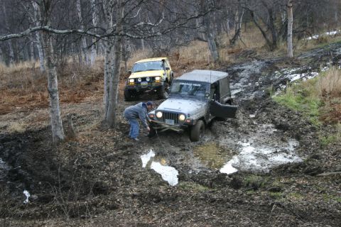 2003 Jeep TJ - Two Jeeps navigate a muddy off-road trail, with one vehicle requiring assistance from a winch.