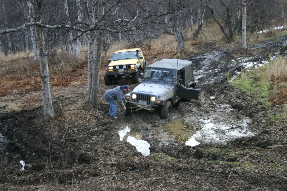 Silver 2003 Jeep TJ being winched out of mud with yellow Jeep in background