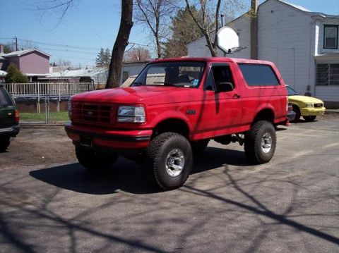 1991 Ford Bronco - Red Ford Bronco with aftermarket wheels and tires parked outside on a sunny day.
