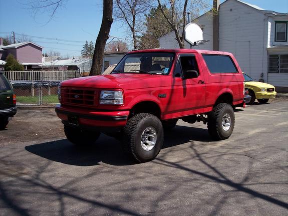 Lifted red Ford Bronco parked on asphalt, yellow car in background
