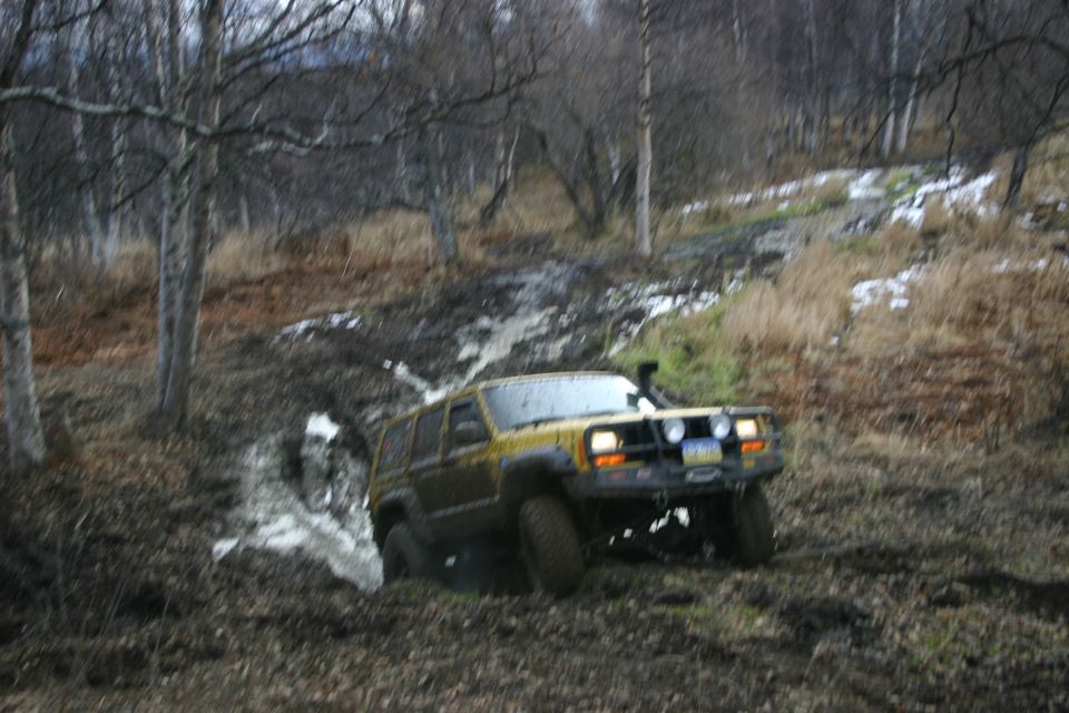 Yellow Jeep Cherokee XJ driving through a muddy, wooded area