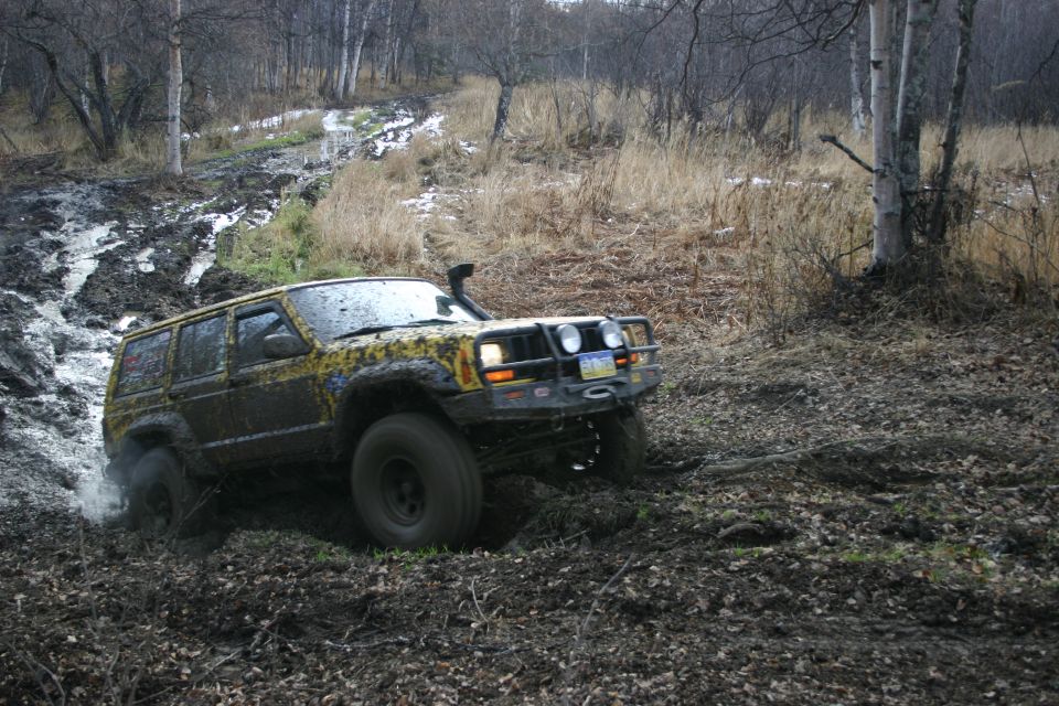 Yellow Jeep Cherokee XJ with snorkel and brush guard driving through mud