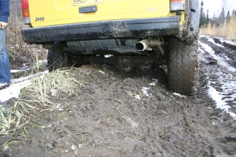 2003 Jeep TJ - A yellow Jeep is stuck in thick mud on a trail with snow patches.