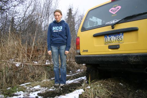 2003 Jeep TJ - A yellow Jeep SUV is parked in a muddy, wooded area with a woman standing next to it.