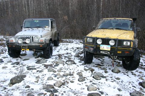 2003 Jeep TJ - Two off-road vehicles, a silver Jeep TJ and a yellow SUV, are parked on a rocky, snow-covered surface.