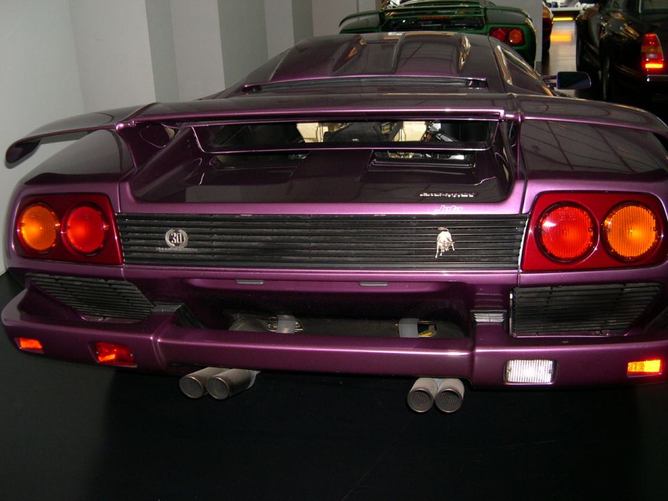 Purple Lamborghini Diablo rear view with quad exhaust pipes and distinctive taillights. Another green car is visible behind it