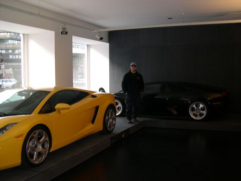 2003 Jeep TJ - A man stands between a yellow and black sports car in a showroom.