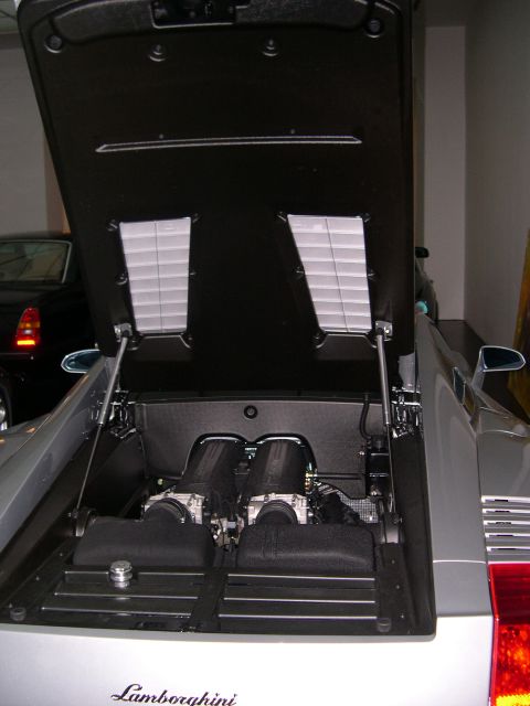 2003 Jeep TJ - The rear engine compartment of a Lamborghini is open, revealing its powerful twin-intake engine.