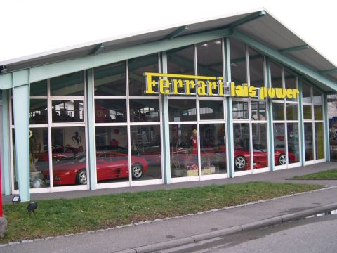 2003 Jeep TJ - Ferrari dealership exterior showing multiple red sports cars displayed inside through large glass windows.