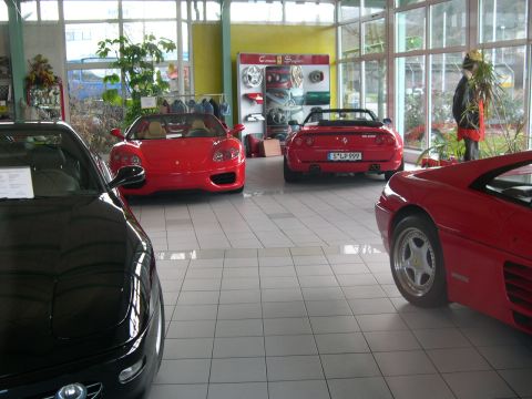 2003 Jeep TJ - Multiple red sports cars are displayed in a bright showroom, with a black car partially visible in the foreground.