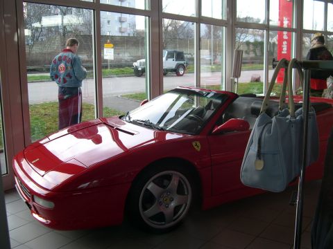 2003 Jeep TJ - Red convertible sports car inside a showroom, with a white Jeep and people visible outside.