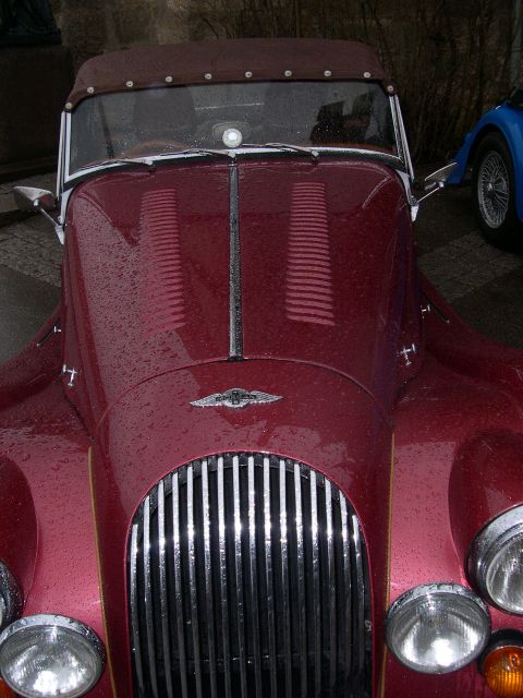 2003 Jeep TJ - A red convertible with a prominent chrome grille and round headlights is seen from the front, with raindrops on its surface.