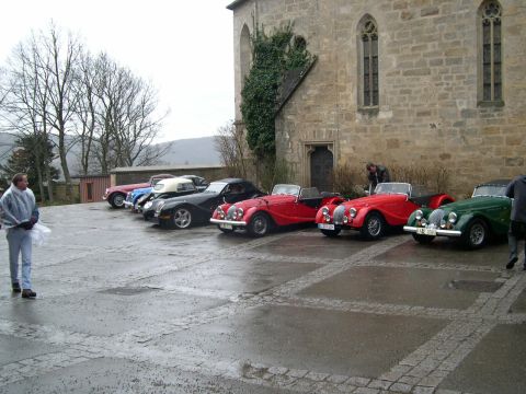 2003 Jeep TJ - A group of vintage sports cars are parked in a line outside a historic stone building on a cloudy day.
