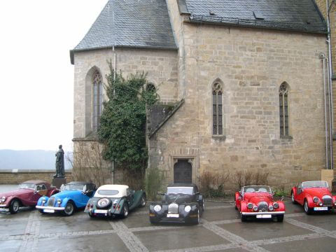 2003 Jeep TJ - A collection of vintage automobiles are lined up in front of an old stone structure.