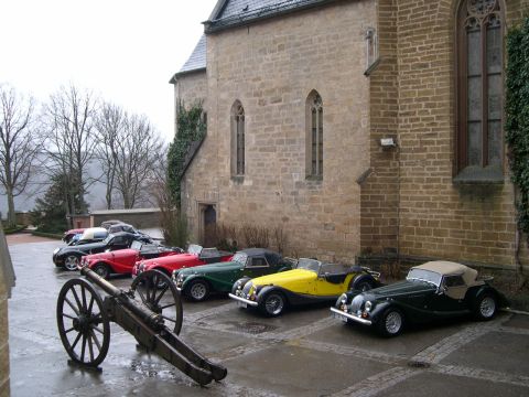 2003 Jeep TJ - A collection of vintage roadsters are parked in a line next to a historic stone structure.