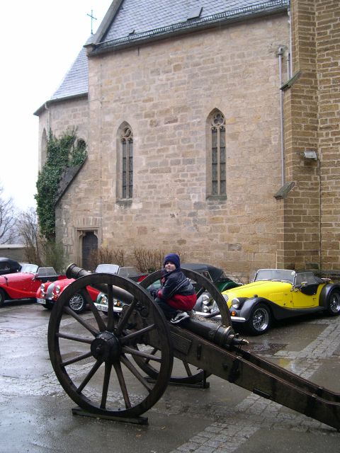 2003 Jeep TJ - A child poses on a historic cannon with a collection of classic cars parked nearby a stone church.