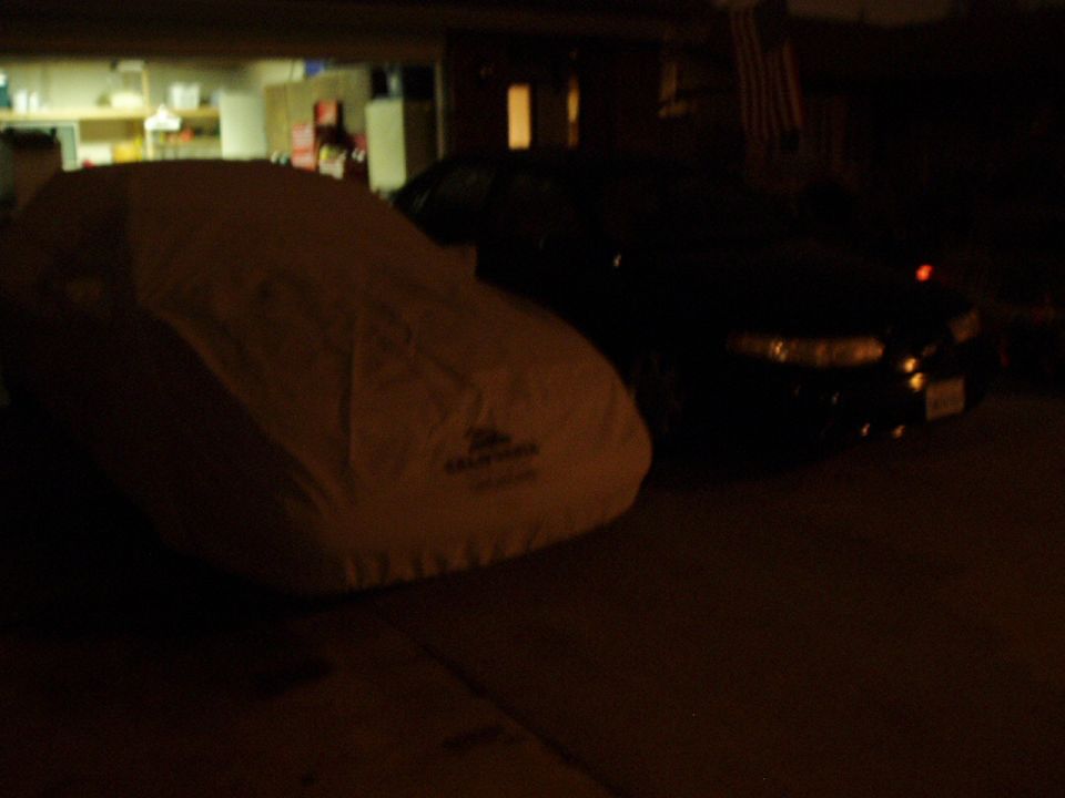 Car cover in front of a black sedan parked in a driveway at night