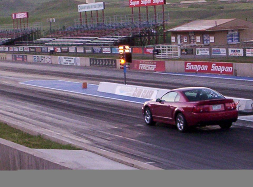 Red coupe on drag strip, rear view. Visible license plate and spoiler